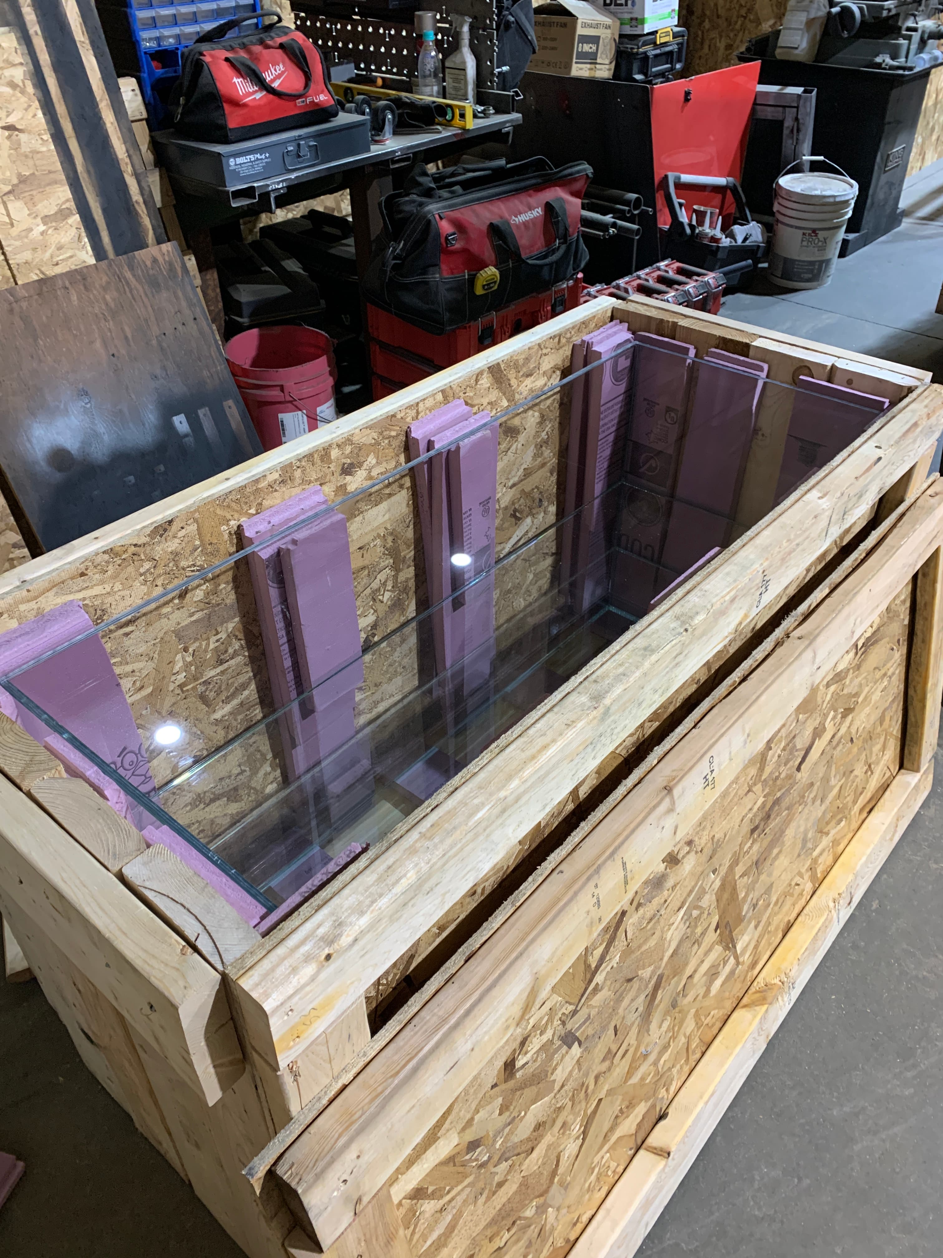 A completed glass display case seated inside an open wooden crate lined with pink protective foam.