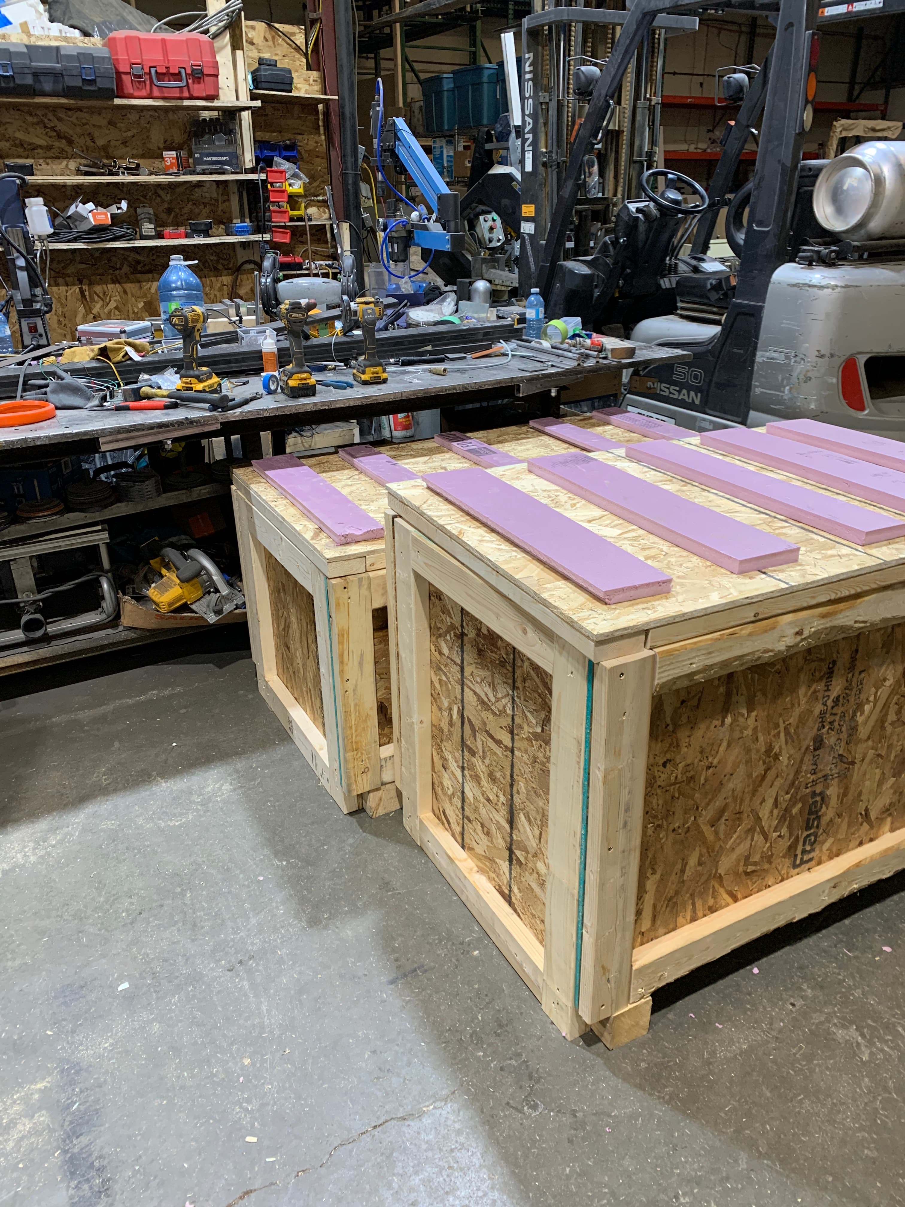 Two purpose-built wooden crates on the shop floor with foam strips laid across the tops, ready to receive product.